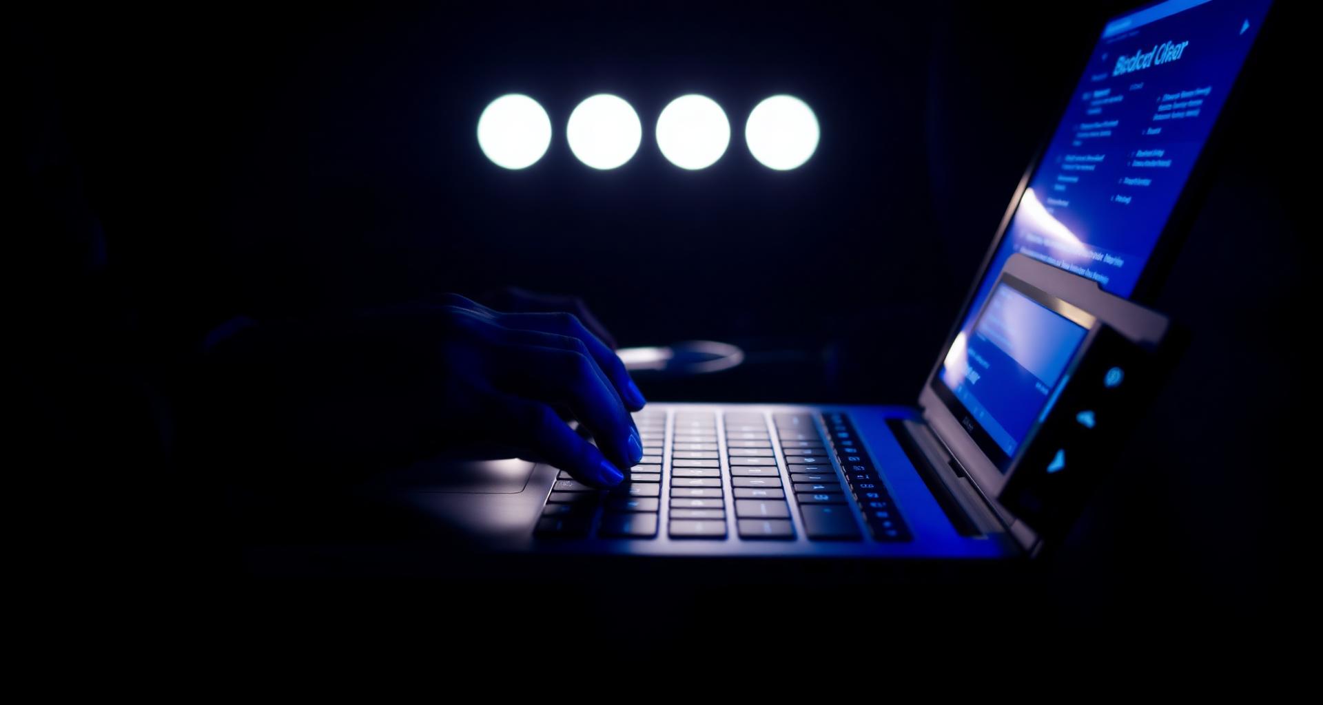 Hands navigating a laptop with assistive technology in a low-light environment